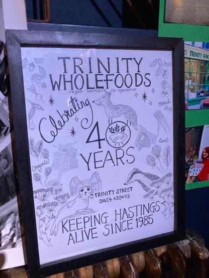 A hand drawn birthday card to "Trinity Wholefoods" includes drawings of badgers and other wildlife, with the message "Celebrating 40 Years. Keeping Hastings Alive Since 1985. 3 Trinity Street. 01424 430473