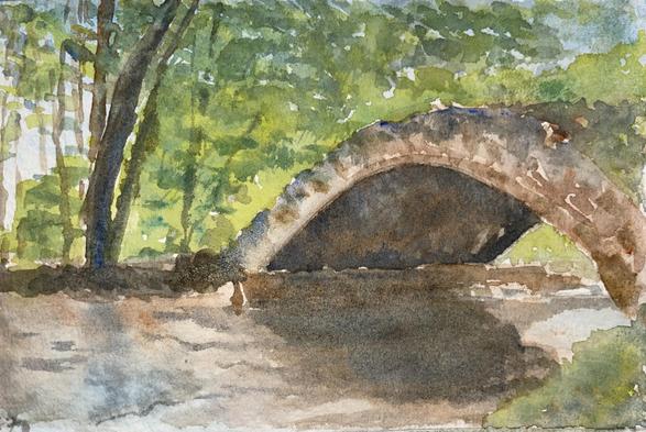 A gently arched stone bridge spans a quiet stream beneath a canopy of trees, with soft light filtering through the foliage and casting dappled reflections on the water below.