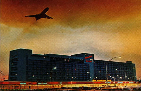 The sun has set and the sky looks like its on fire. There is a plane taking off over the terminal and hotel at Miami.