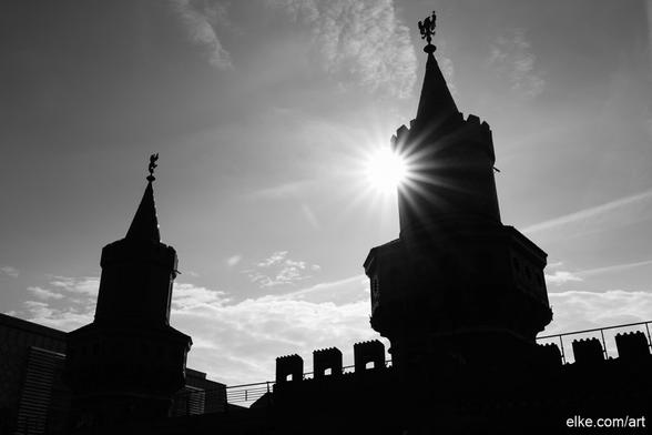 A dramatic silhouette of Berlin’s Oberbaum Bridge (Oberbaumbrücke), captured in striking black and white as the sun pierces through its historic turret.

The neo-Gothic structure, once a border crossing between East and West, now stands as a powerful symbol of unity and transition. With bold contrasts and radiant light beams, this photo transforms architectural history into visual poetry. A timeless capture of Kreuzberg’s most iconic bridge.

Ideal for modern interiors, urban-themed spaces, or photography collections with historical depth.

Perfect for collectors of Berlin imagery, monochrome art lovers, or fans of architectural symbolism.