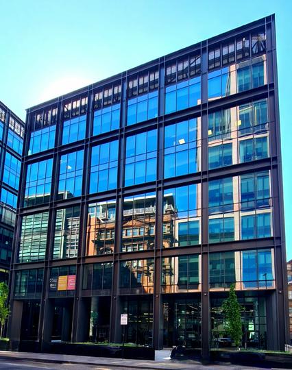 The facade of a traditional red sandstone build reflected in the glass front of a modern building.