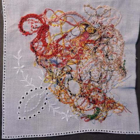 Ein paar Fadenreste aus der textilen "Mülltüte" werden auf einem Viertel eines Taschentuchs zum Umhäkeln aufgenäht.