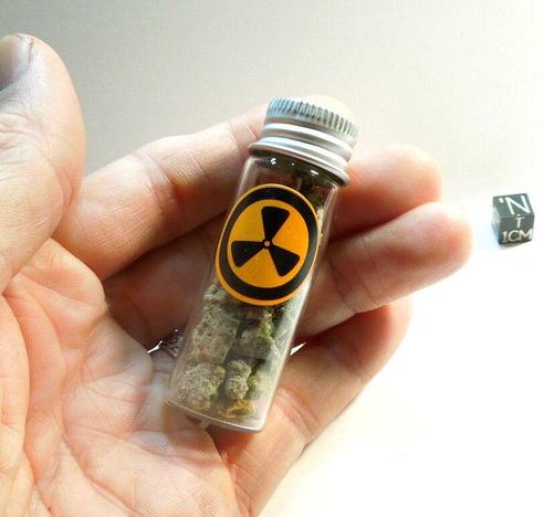 A glass vial of trinitite fragments with a radioactive symbol decal on it.