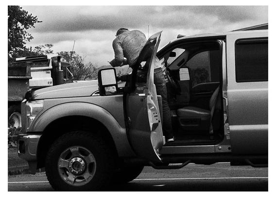 Taking a photo of something around the hood of their pickup. At least I hope it is their truck. Might be getting the Vehicle Identification Number idk. Life in the rural USA documentary street photography in black and white.