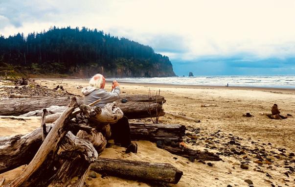 Different camera, different view. A Photographer taking a photograph while perched on Driftwood at Cape Meares Oregon.