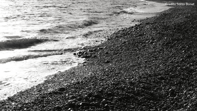 Kieselstrand und Wellen im Gegenlicht am Ufer in Cartagena, Murcia.
Oben rechts steht: "Credits: Sonia Bonia"