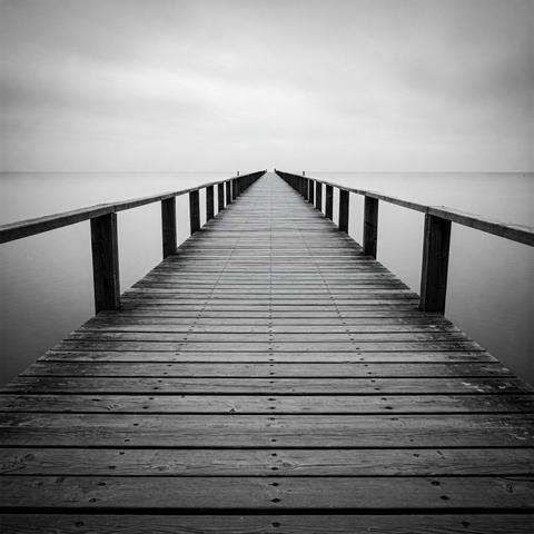 An atmospheric black and white photo of a pier and the sea in a calm, minimalist style.