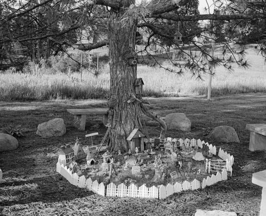 A tree encircled by a miniature picket fence within which is nestled a tiny village.