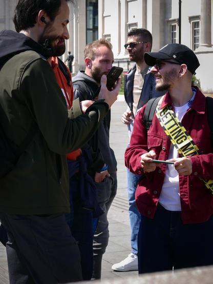 A man in his thirties or thereabouts, dressed in a red jacket, black trousers, and a black baseball cap, and with a ginger beard, glasses, and an earring, with a "Getting Married" sash over his right shoulder, stops off at Trafalgar Square with his stag party, on their way via "all the bars in London" to some distant back street where he will possibly be divested of his trousers and padlocked to a lamp post. OK, I made up the last bit.