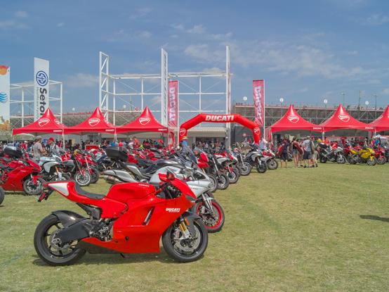 Some Ducati motorcycles lined up at Ducati Island with red Ducati tents and an archway in the foreground