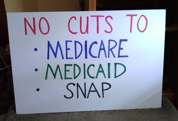 A white protest sign that reads, " No Cuts To Medicare, Medicaid, Snap."