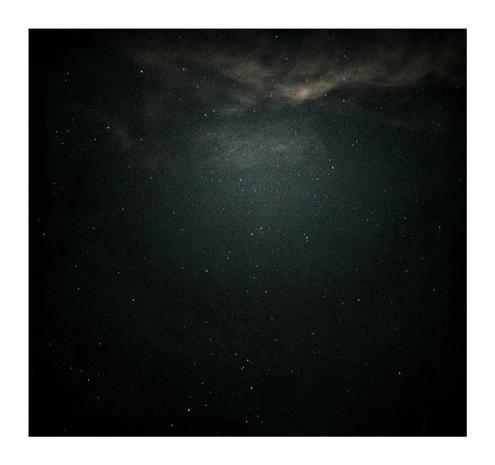 The photo is of a starry night sky, with a dark background and numerous white dots scattered throughout - which are the stars. The top portion of the image features a cloudy section that is has a yellow/green tinge to it.