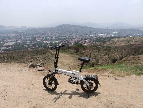 A photo of my ebike parked on the dirt road with the view of a densely populated hill in the background