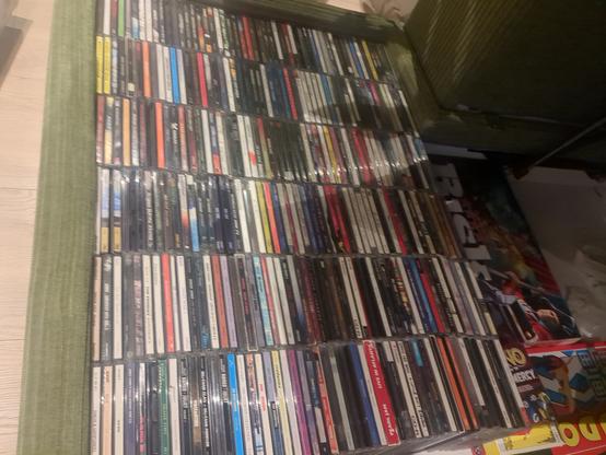 A green sofa with storage inside is filled with CDs music.