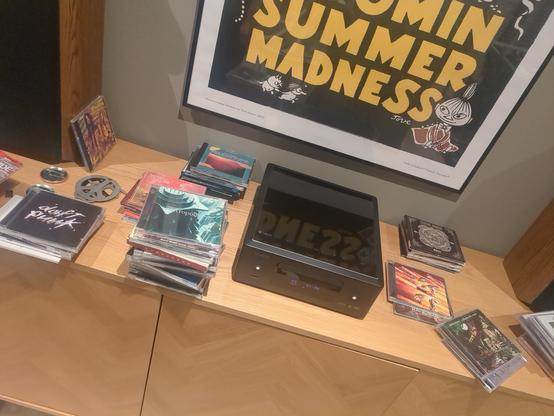 A wooden surface with a denon music player ontop filled with CDs laying around it.