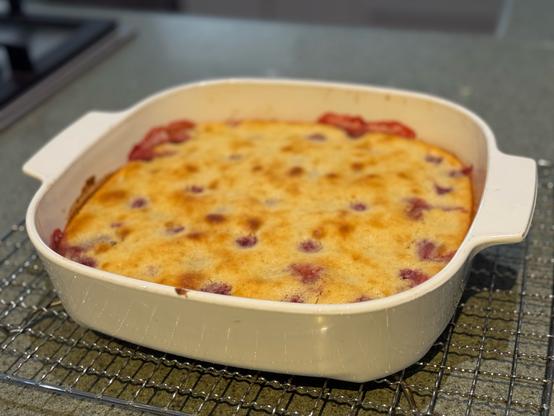 A square baking dish with a lightly browned cake dotted inside with raspberries and strawberries.