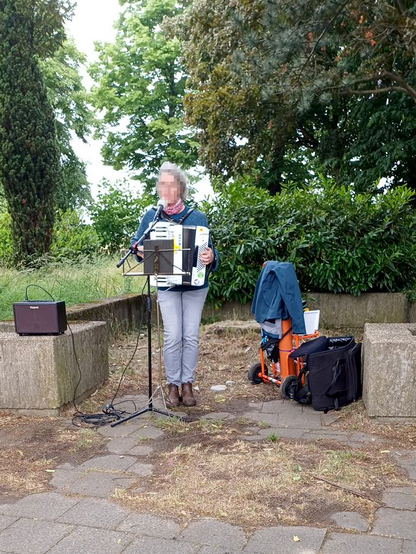 Eine Musikerin singt zum Akkordeon, imHintergrund Bäume und Büsche