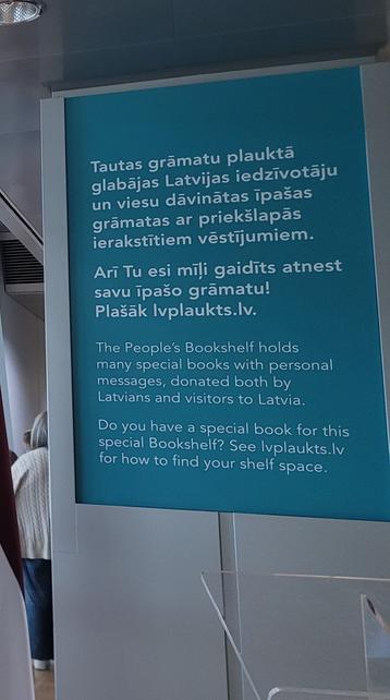 Foto of an information board reading: 
The People's Bookshelf holds
many special books with personal
messages, donated both by
Latvians and visitors to Latvia
Do you have a special book for this
special Bookshelf? See lvplaukts.lv
for how to find your shelf space