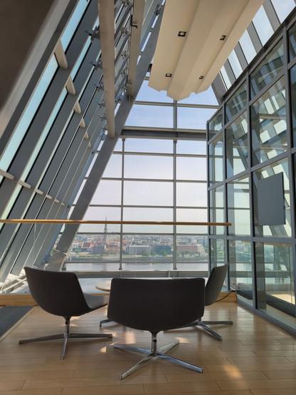 View from the pointed shaped glass tip on the 12th floor. You see a few comfy chairs so you can sit down to enjoy the view. You see across the river and look towards Rigas old town center