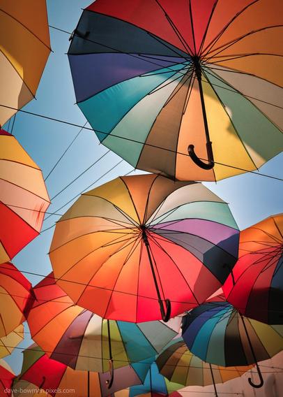 A photograph of colourful umbrellas hanging above a side street in George Town, Penang, Malaysia, set against a clear blue sky. Taken from below, the umbrellas fill the frame with vibrant colours, creating a bright and cheerful atmosphere.