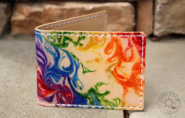A handmade leather wallet. The shell is undyed leather with rainbow marbling and white stitching. Front view.