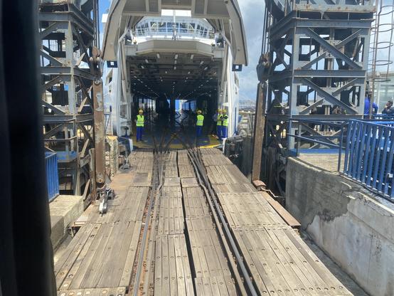 The open jaws of a ferry ready to swallow a train in three bites.

in the foreground, a wooden deck with rails.  In the centre, the train deck of a ferry is visible with light at the far end