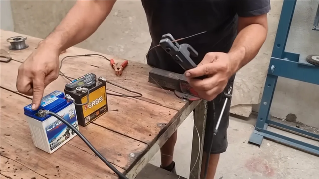 [ImageSource: Professor Bardal]

In this case, the current is provided by a pair of 12-volt motorcycle batteries hooked together in series. There’s also a torch of sorts — a short length of copper capillary tubing with a 1-mm inside diameter clamped in the jaws of a stick welder stinger, or a pair of locking pliers if you’re really in a pinch. The torch is connected to the negative terminal on the battery with a jumper cable, and the positive terminal is connected to the workpiece.

To create the weld, a piece of 0.8-mm flux-core welding wire is threaded through the capillary and into the joint, and fed by hand as it’s consumed. It’s awkward and awful, but it works. Of course, there’s no control over amperage as there would be with a legit welding machine, which would make it hard to adapt this method to different materials. Weld quality appears poor, too. But I suspect that if you were in a position to need a welder like this, you wouldn’t really care about any of that.