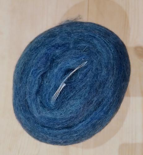 Spinning fiber in a heathered turquoise colorway. It is wound into a something the resembles a yarn cake.