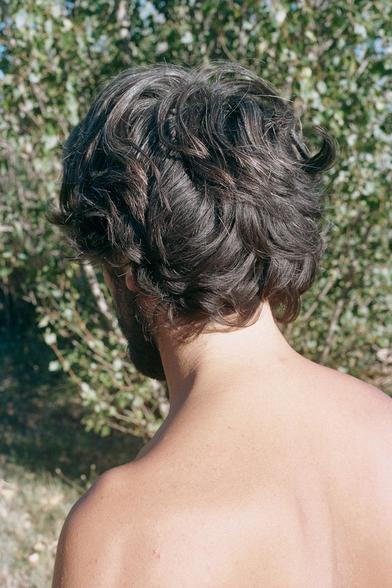 #4, excerpt from the series Regrets by Stefano Marchionini, c. 2018 and ongoing (photography) is an outdoor photograph of a young man's back in the sunlight, hair shaggy and dry.