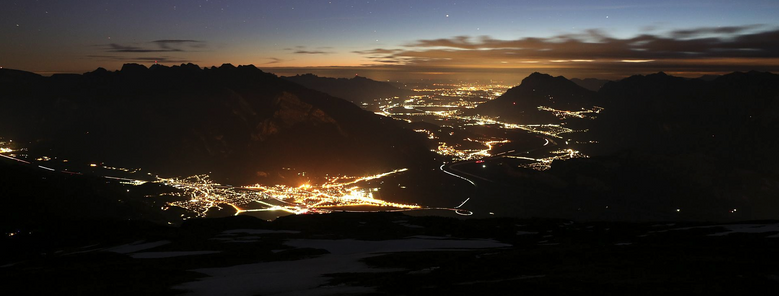 Nachtaufnahme mit Bergen und Ortschaften im Tal.