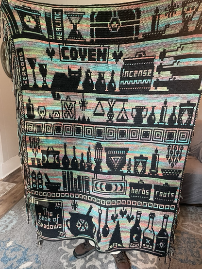 Witches bookshelf crochet blanket. 6 shelves that are loaded with books, potions, bottles, a black cat, and all sorts of witchy paraphernalia.