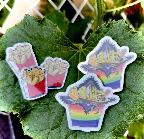 using a cucumber leaf as a display, two sets of stickers are shown. a progressive pride fry sticker with holographic edge and extra fries with holographic edge