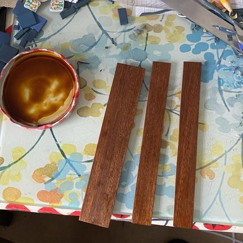 Three partially polished pieces of a fire surround on a glass placemat with a jam jar lid with a little French Polish dispensed into the lid.
