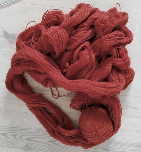 Brick red wool yarn - some of it still in skeins, some already wound into a ball. Everything tumbled together from an overturned basket.