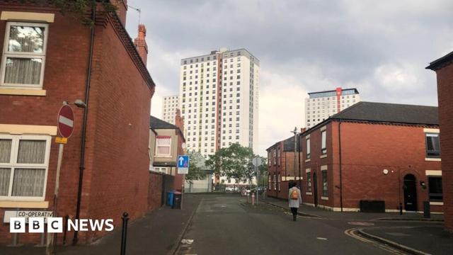 Tower blocks can be seen in the distance, behind rows of terraced red brick properties. A road sign on the left says Co-operative Street.