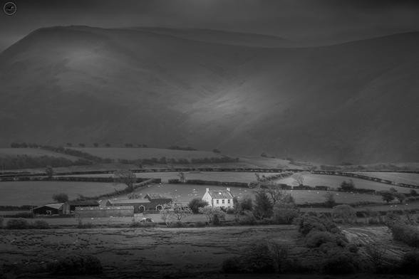 monochrome shot of farm house and buildings against mountain backdrop