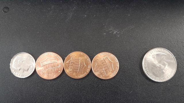 A dime and three pennies all in a line centered and touching and a quarter off to the side