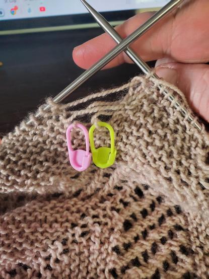 Close up of pinkish grayish yarn knitting on circular needles, with laddering down about 4 rows underneath dropped stitches.