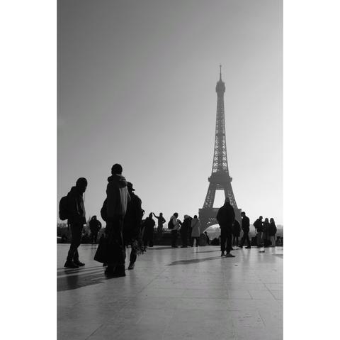 Black and white street photography taken on the Trocadero square in Paris. Vendors and tourists silhouettes  stand in front of the Eiffel tower, in a back-lit hazy atmosphere.