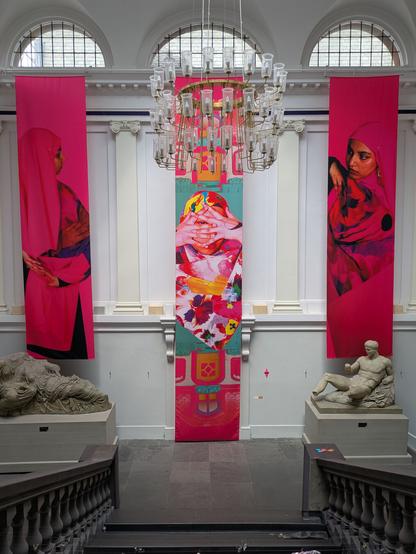 Three large silken banners in bright magenta hues hang from a large stairway