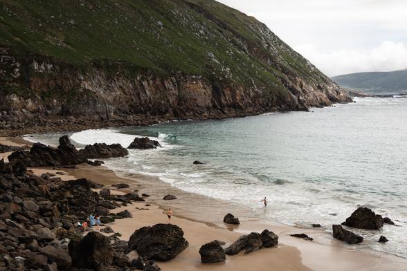 two people run into the ocean as their partners get ready for a swim at Keem Beach in Ireland