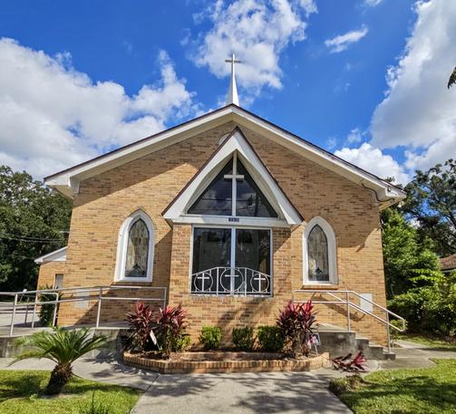 Front view of a brick church with large stained glass windows in front and a Christian cross on the roof.