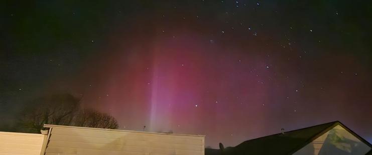 Photo of the aurora, with one or two main beams of light on the center left.  There are various other beams of different strengths extending out to the right, painting the sky red/magenta.