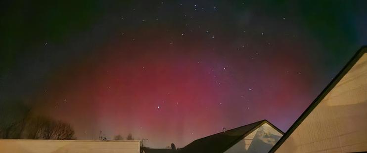 The aurora is mostly a reddish arc across most of the night sky, extending up from the bottom of the photo.  Near the bottom (above the neighbouring rooftops) the colour changes to a pale green.