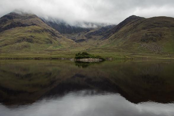 a very small island in the middle of a lake, surrounded by mountains