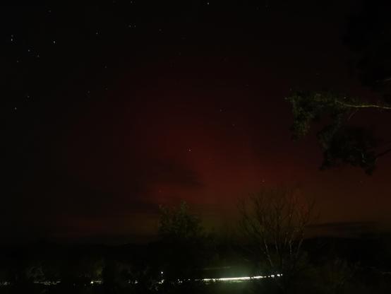 Red aurora with a little bit of green near the horizon. There is a streak of light from car headlights underneath