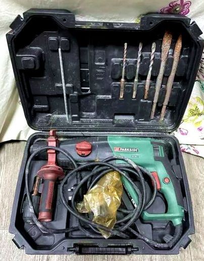 A used Parkside hammer drill in a black moulded suitcase. The tool is in the bottom, the cable a losely coiled up mess whose loops are escaping, making the box hard to close. The lid still holds the five tools it came with, there's no space for storing more drill bits or chisels. A plastic drill chuck is clamped in the bottom part, too.

[photo from the Internet, because I don't have this tool]