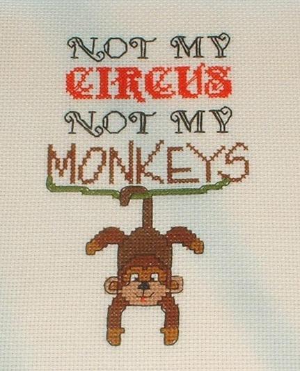 a piece of cross stitch with the words "Not my Circus, Not my Monkeys" in various fonts above a vine hanging between the first and last letters of the last word with a monkey hanging upside down off the vine by his tail.
