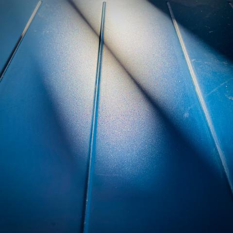 Close-up of a textured blue table surface with subtle reflections of sun light, creating a gradient effect.