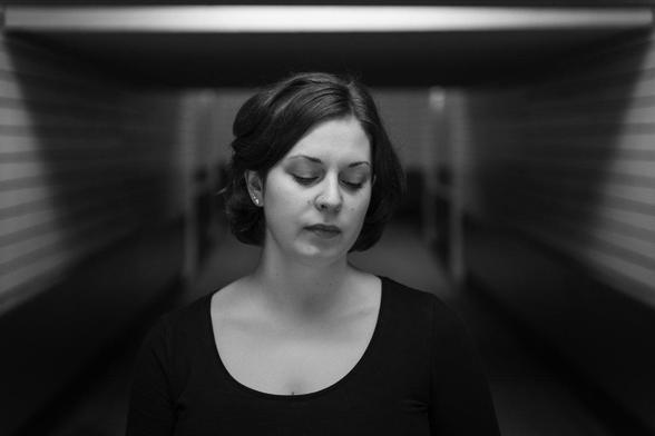 Brustportrait einer Frau, die in einer Unterführung steht und seitlich zu Boden schaut.